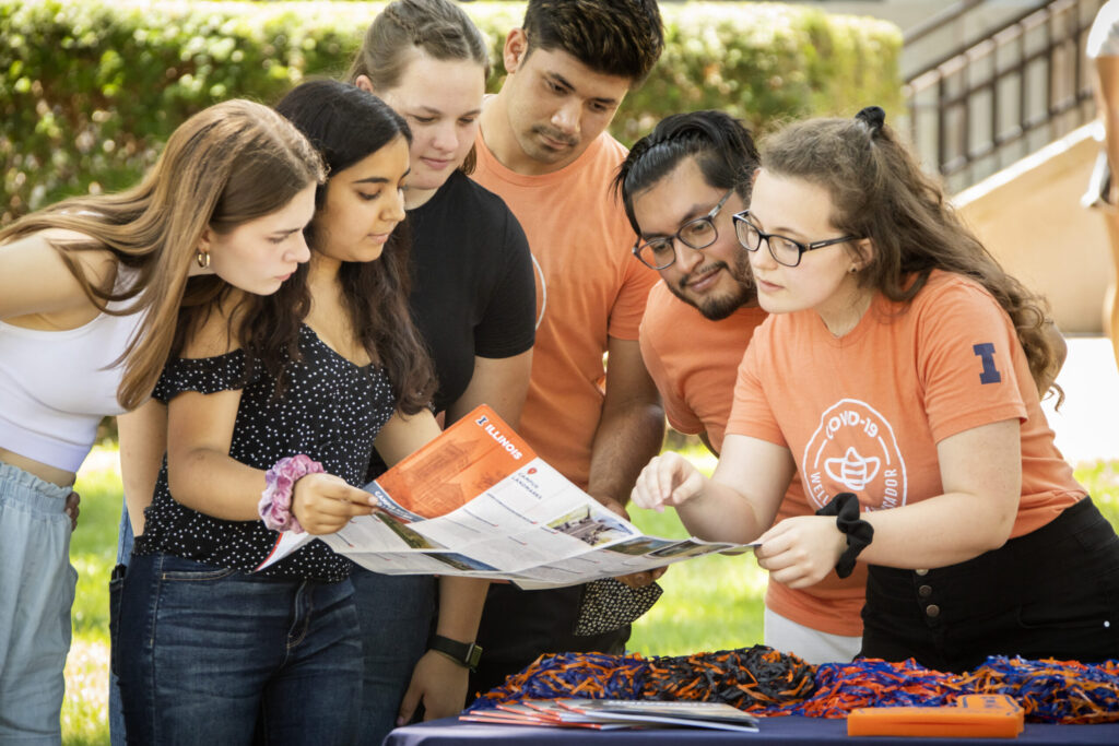 Female undergraduate students take directions while looking at a campus map from COVID-19 Wellness Ambassadors in front of the English Building.